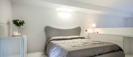 A modern bedroom with a bed, bedside table, and a nightstand with a lamp.