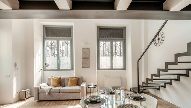 A dining area with a glass table set for four, a sofa, and a staircase. - Porta Torre Lofts (Como)