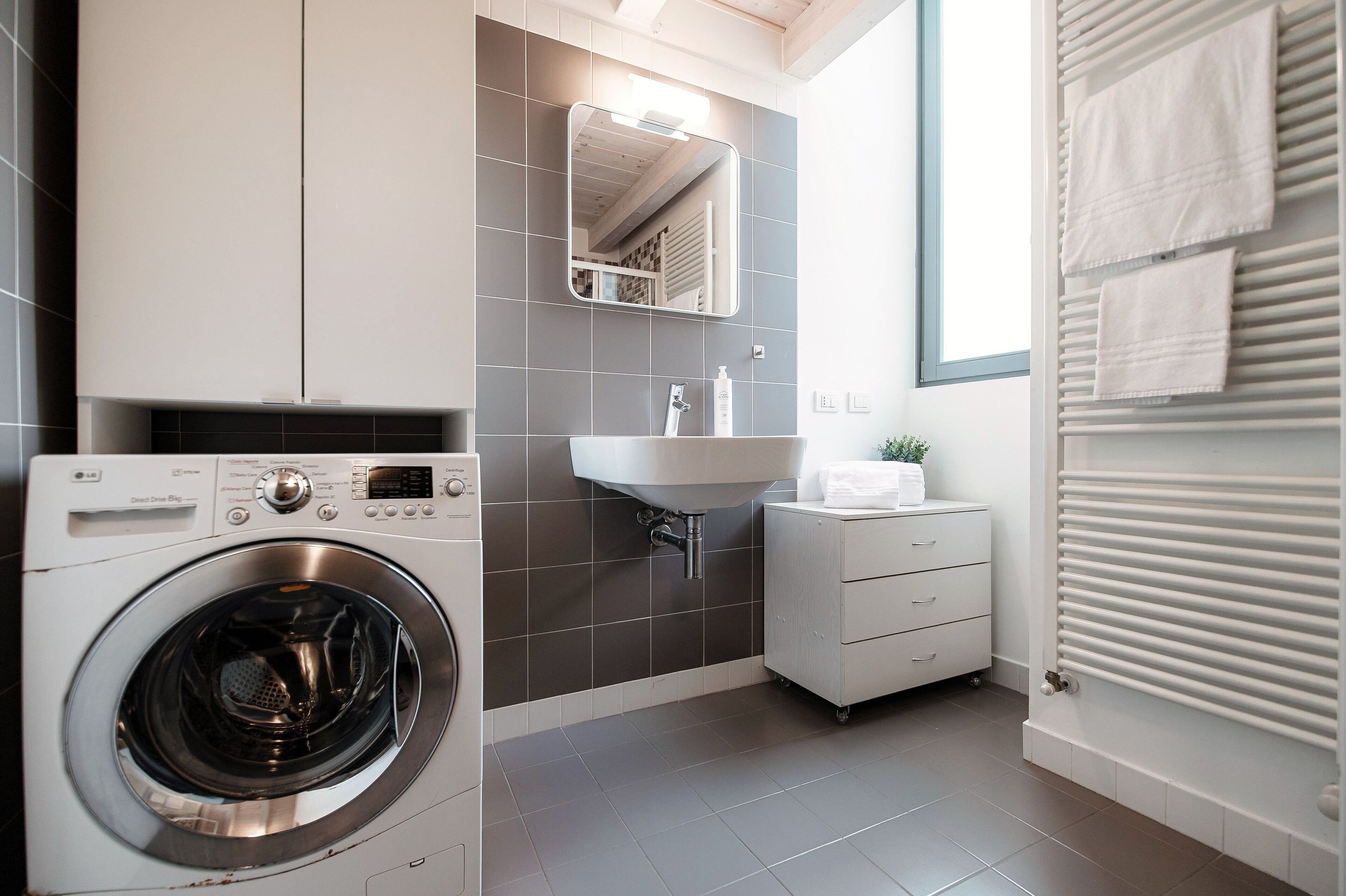 A modern bathroom with a washing machine, a sink, and a radiator.