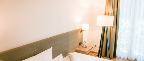 A hotel room with a bed, a nightstand, a lamp, and a window with curtains.