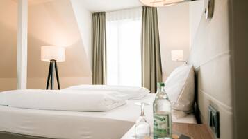 A hotel room with a neatly made bed, a bedside table with a bottle and glass, and a lamp.