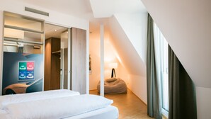 A modern hotel room with a bed, a desk, a bean bag, and a large window with curtains. - Hotel Trezor (Singen)