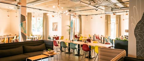 A modern dining area with a mix of seating options including a long communal table and individual booths, surrounded by colorful chairs.