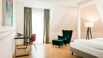 Una habitación de hotel moderna con cama, escritorio, dos sillas y lámpara.