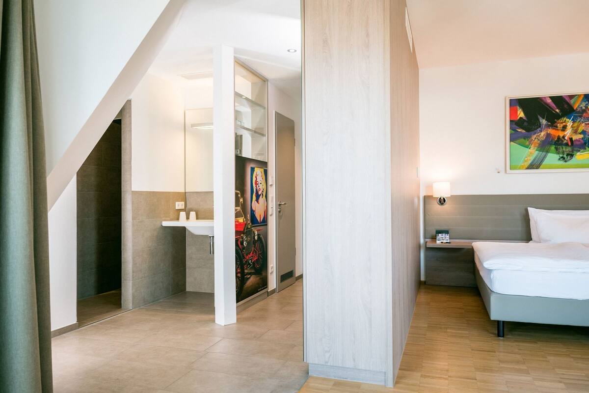 A hotel room with a bed, bedside table, and a painting on the wall.