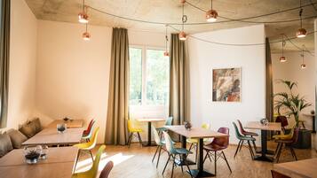 Un comedor moderno con mesas de madera y sillas coloridas, ventanas amplias con cortinas e iluminación colgante.