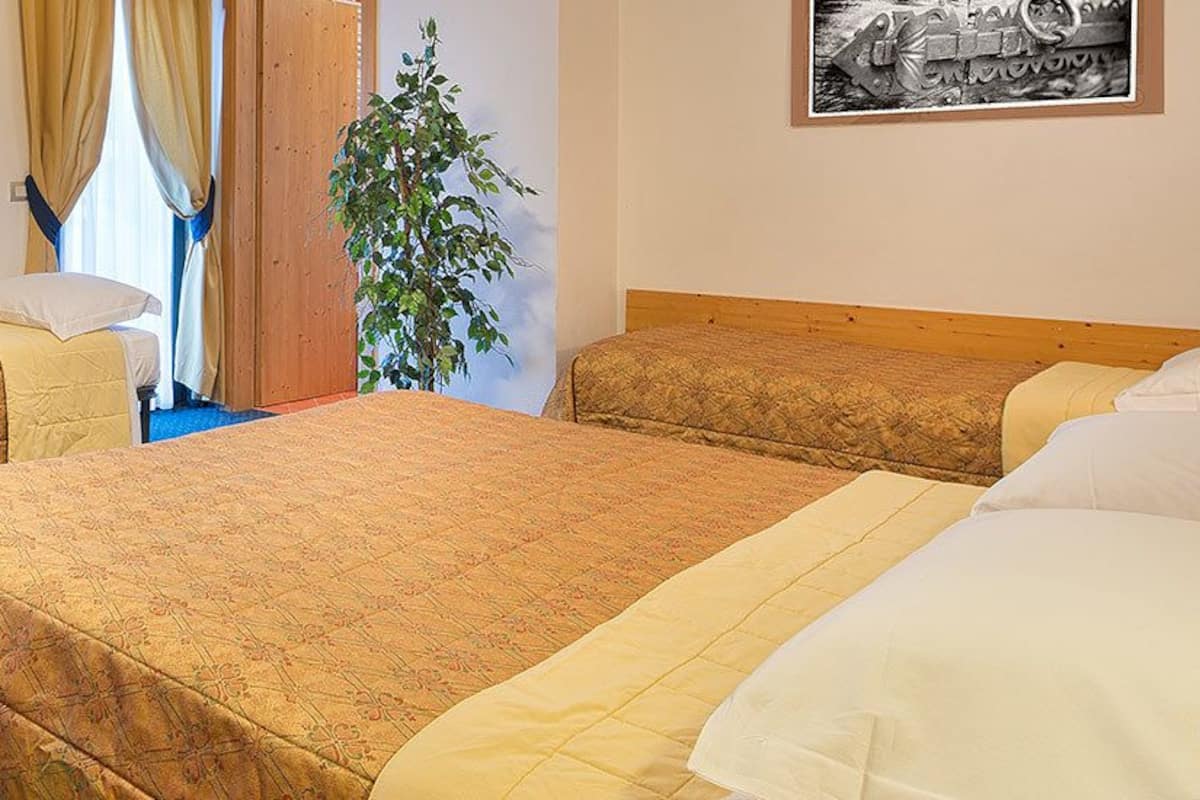 Habitación de hotel con dos camas individuales, un escritorio con una computadora portátil, una silla y un radiador.