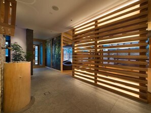 Un interior moderno con un separador de madera con listones, una mesa de recepción y una pared con un mural de bosque.