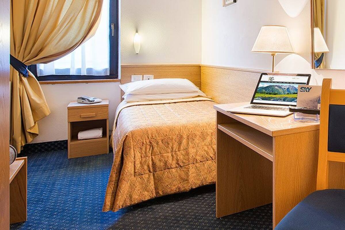 Habitación de hotel con cama, escritorio, ordenador portátil, mesita de noche y baño con inodoro, lavabo y ducha.