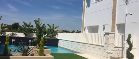 A modern house with a swimming pool, surrounded by a well-maintained lawn and tropical plants.