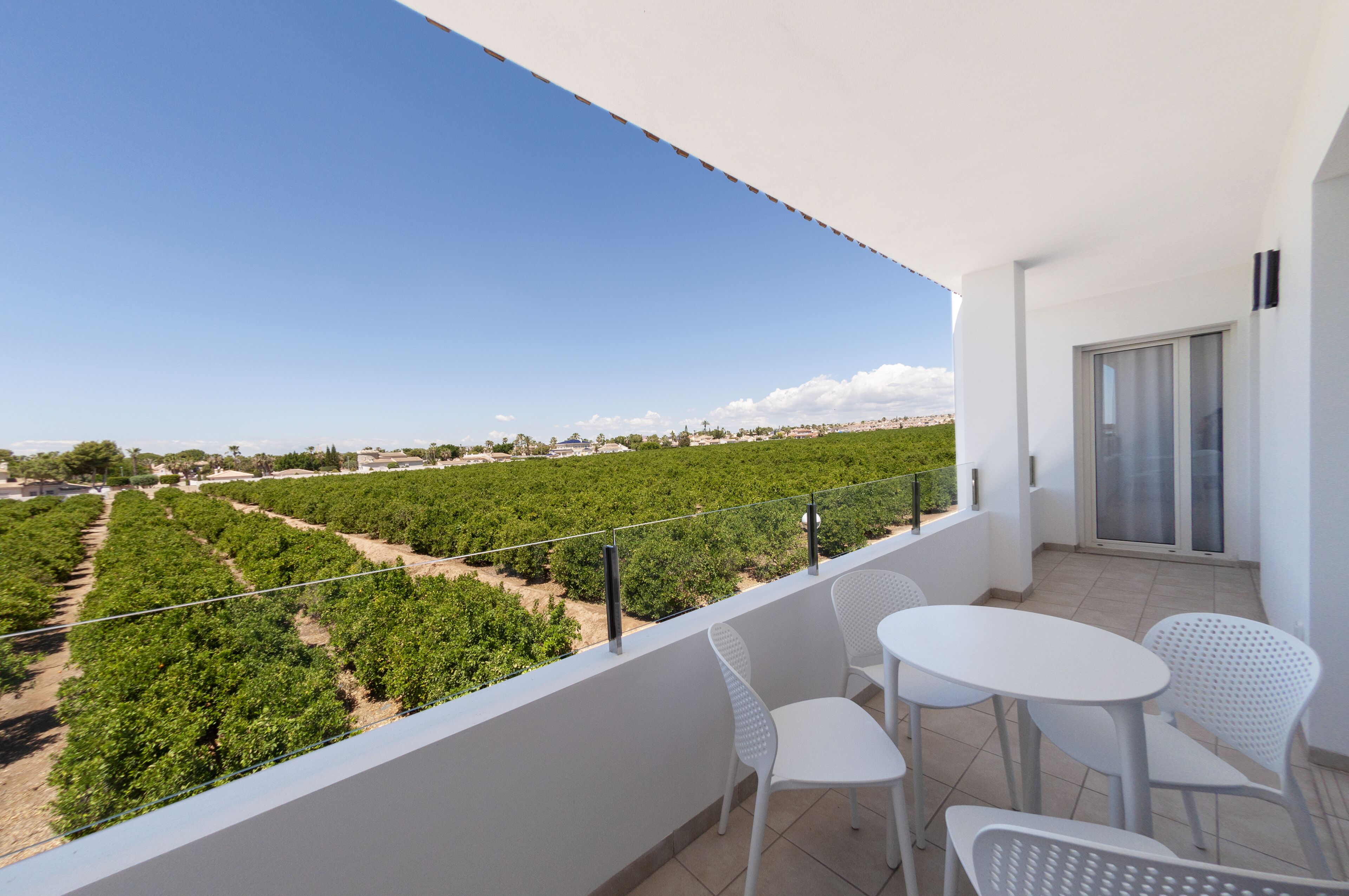 Een balkon met witte stoelen en een tafel, met uitzicht op een wijngaard.