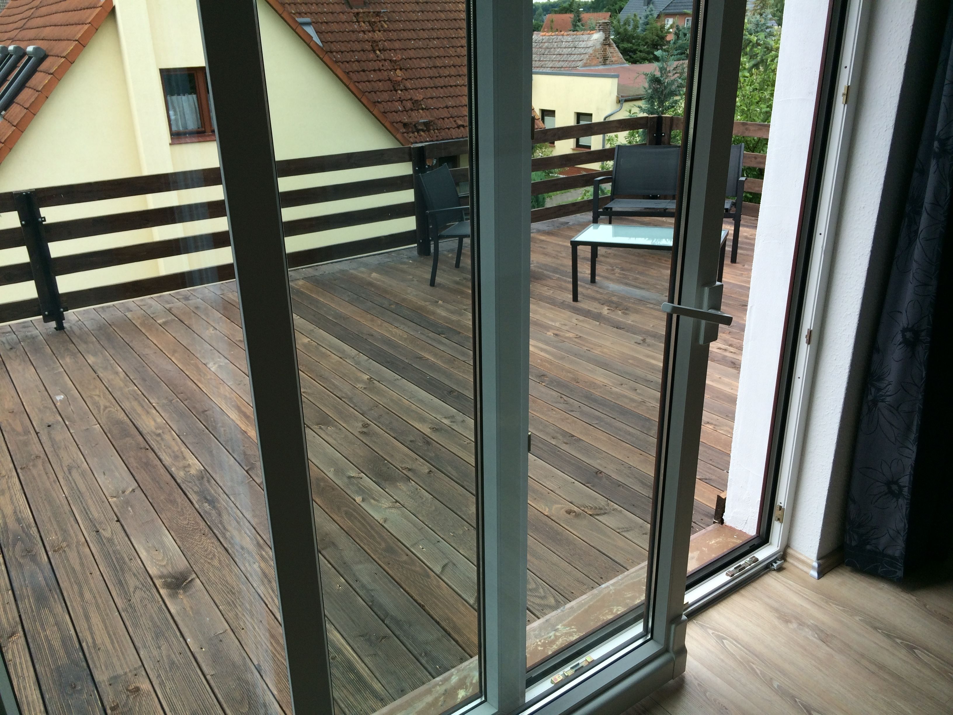 A wooden deck with a glass door leading to an outdoor seating area.