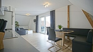 A modern living room with a sofa, a dining table, and a kitchen area. - Haff-Ostseeferienhaus (Monkebude)
