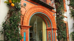 Um edifício tradicional com uma entrada em arco ornamentada, uma varanda com grades de ferro forjado e vegetação exuberante cobrindo as paredes.
