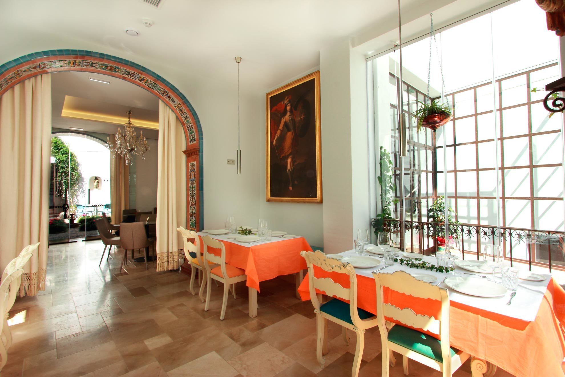 A dining area with tables set for two, featuring orange tablecloths and white chairs.