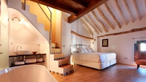 Quarto com uma cama grande, banheiro com banheira e escada que leva a um andar superior.
