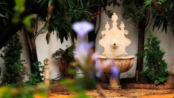 Jardí amb una font de pedra al centre, envoltat d'una varietat de plantes i arbres.