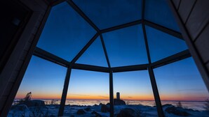 Una stanza con una grande finestra che offre vista su un paesaggio innevato e un tramonto.