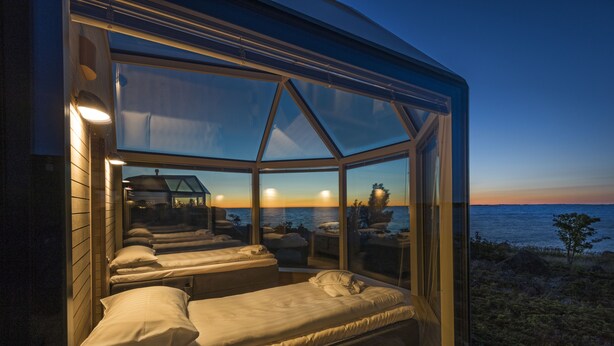 Una stanza con ampie vetrate, due letti, vista sul mare e un tramonto.