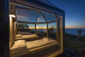 A glass-enclosed room with two beds, a view of the sea, and a sunset. - Kalle's Inn Glass Houses (Korsholm)