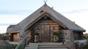 A log cabin with a steeply pitched roof, a wooden door, and a small porch with steps leading up to it. - Kalle's Inn Glass Houses (Korsholm)