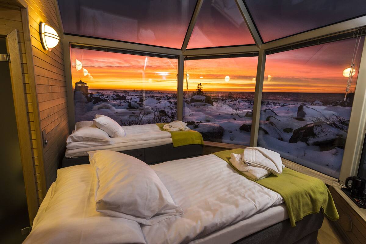 A room with two beds, a view of a snowy landscape, and a sunset.