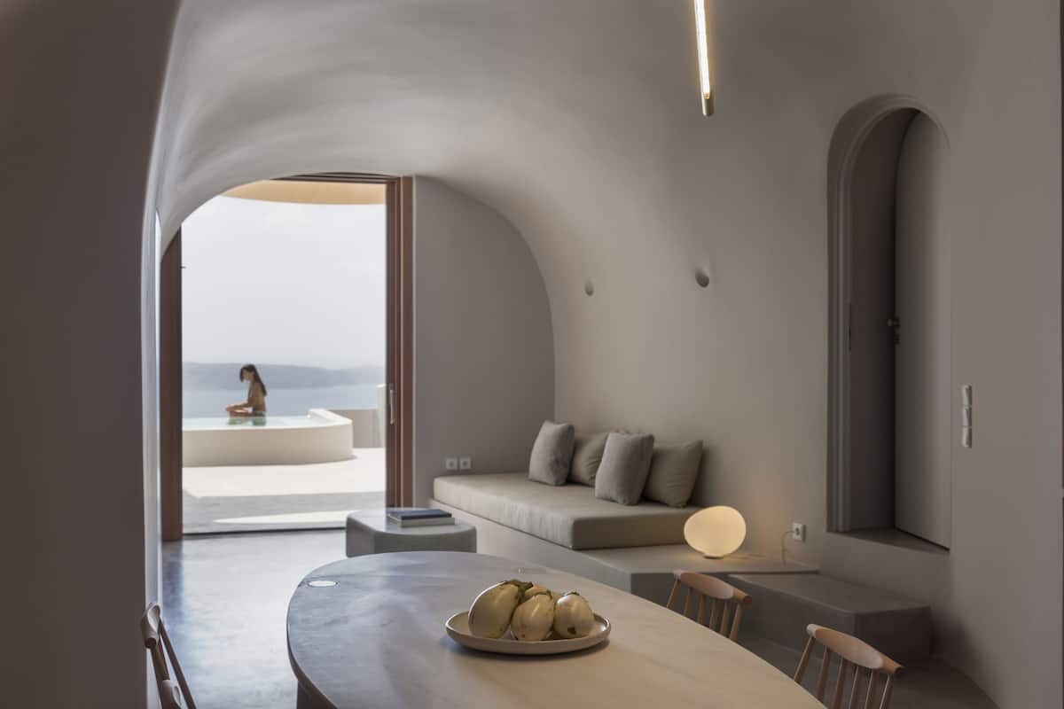 A modern interior with a dining area, a sofa, and a view of the sea.