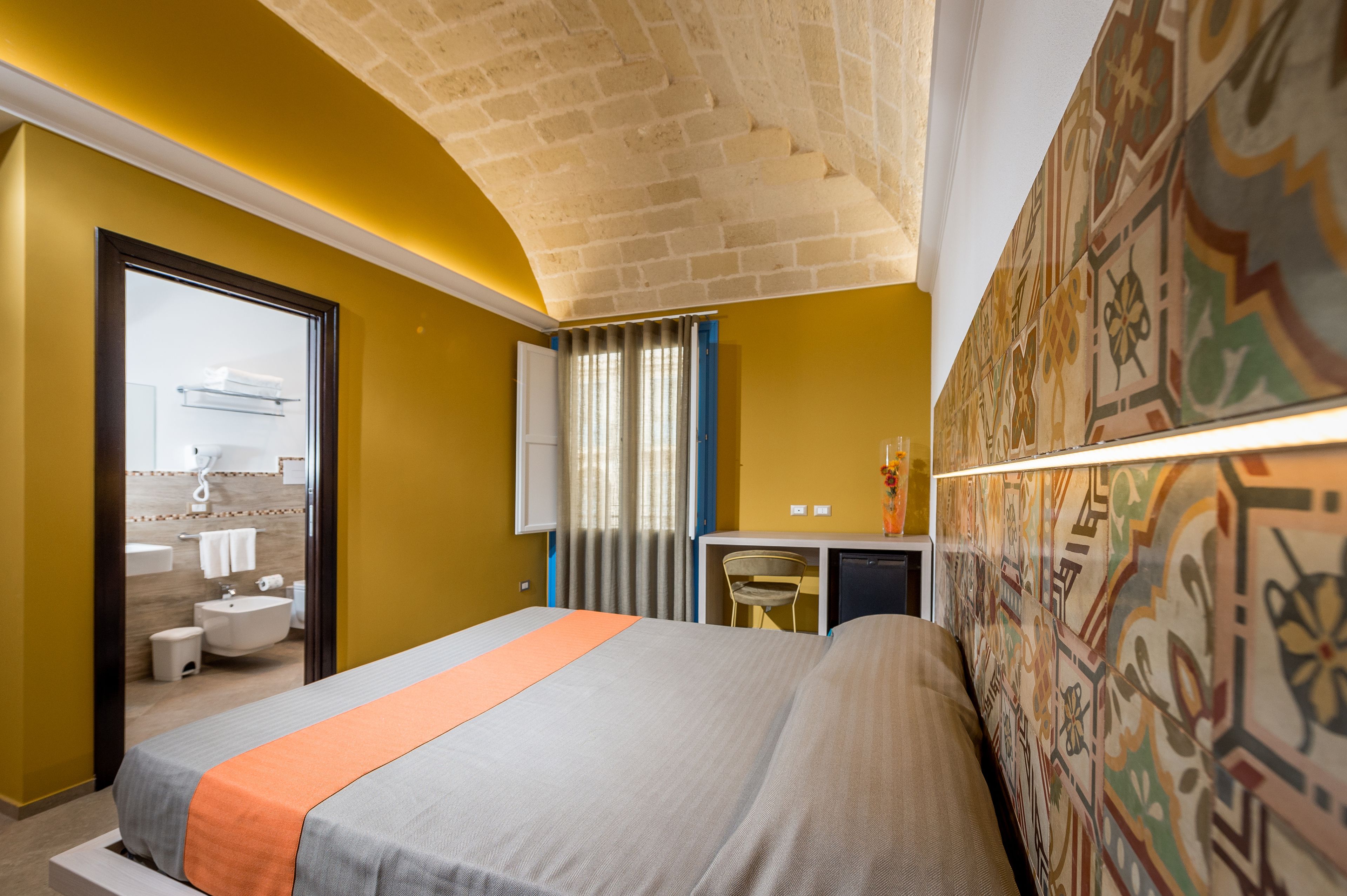 A hotel room with a bed, a desk, a chair, a bathroom, and a decorative wall.