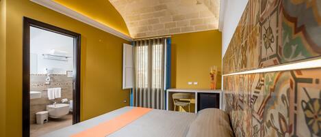 A hotel room with a bed, a desk, a chair, a bathroom, and a decorative wall.