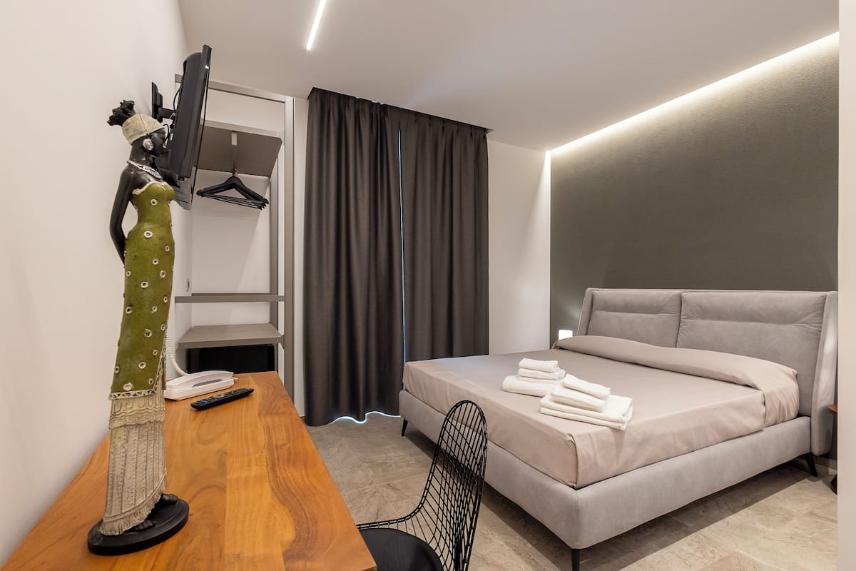 A modern hotel room with a bed, a desk with a computer, a chair, and a TV.