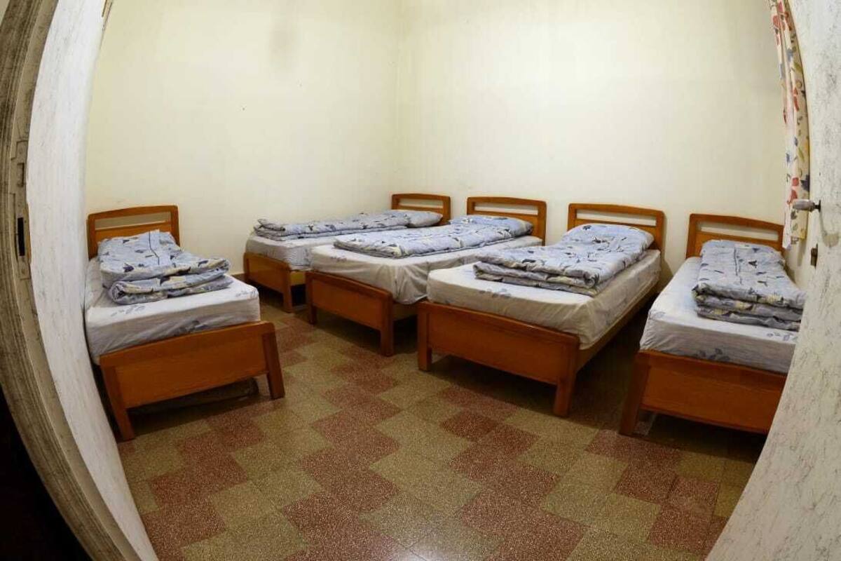 Une chambre de dortoir avec quatre lits en bois disposés en rangée, chacun étant muni d’un matelas et d’une couverture.