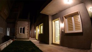 Vista nocturna de un edificio con ventanas iluminadas y un camino que lleva a una puerta.
