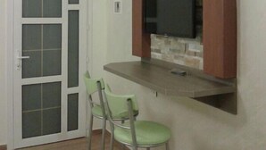 Una habitación con pared de piedra, un televisor de pantalla plana sobre una encimera y dos taburetes verdes.