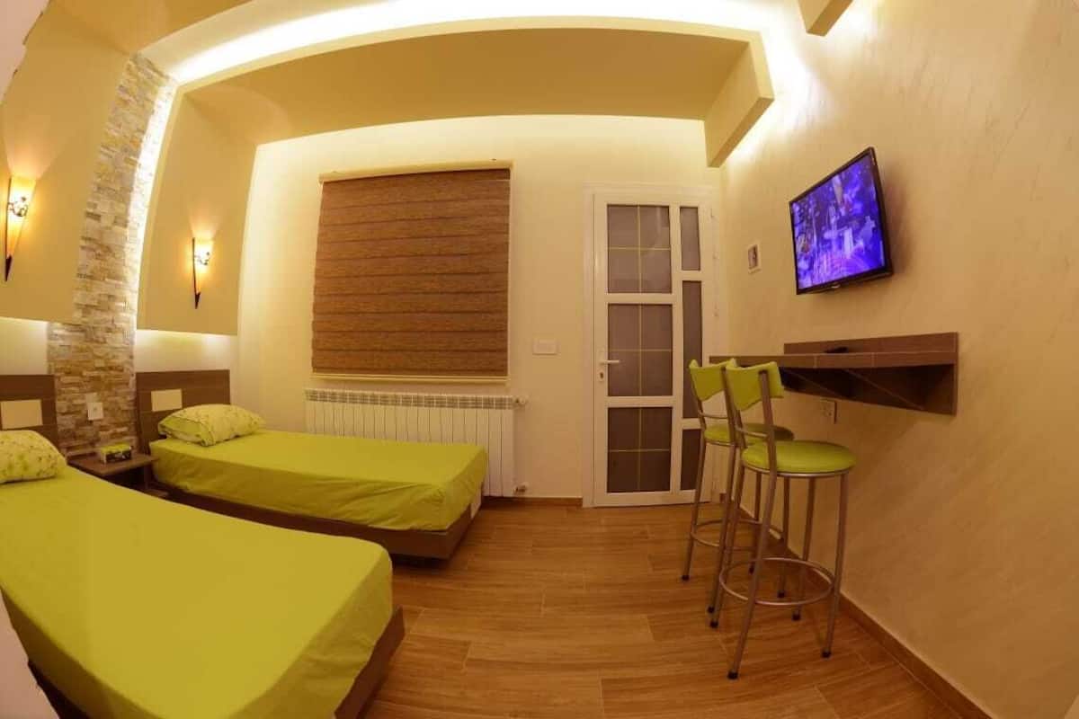 Une chambre de taille modeste, équipée de deux lits, d’une télévision et d’un petit coin bar.