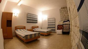 Un dormitorio con dos camas individuales, un armario, un radiador y una pared de piedra.