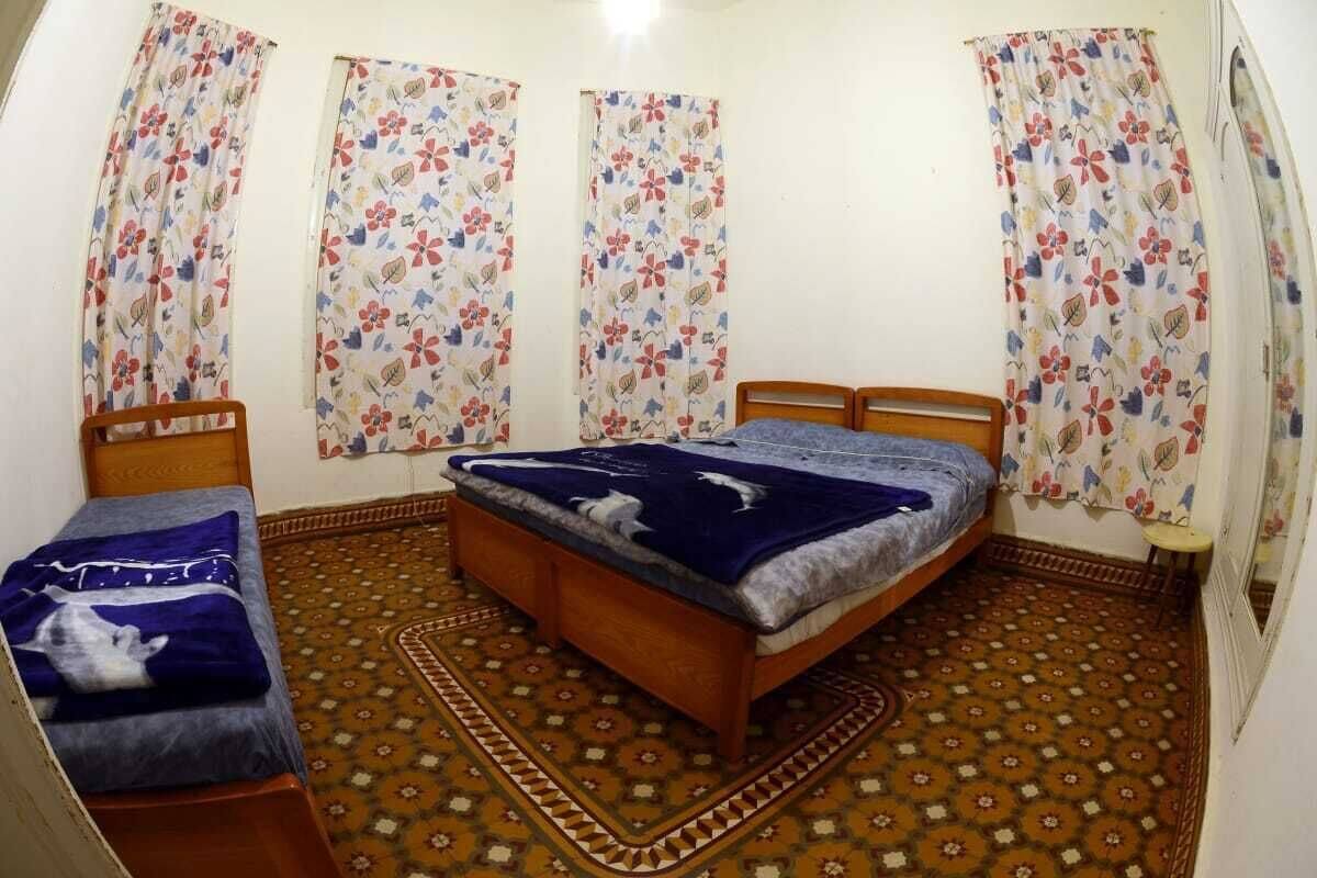 Une chambre avec un lit simple, un plus petit lit ou un canapé, et un tapis à motifs.
