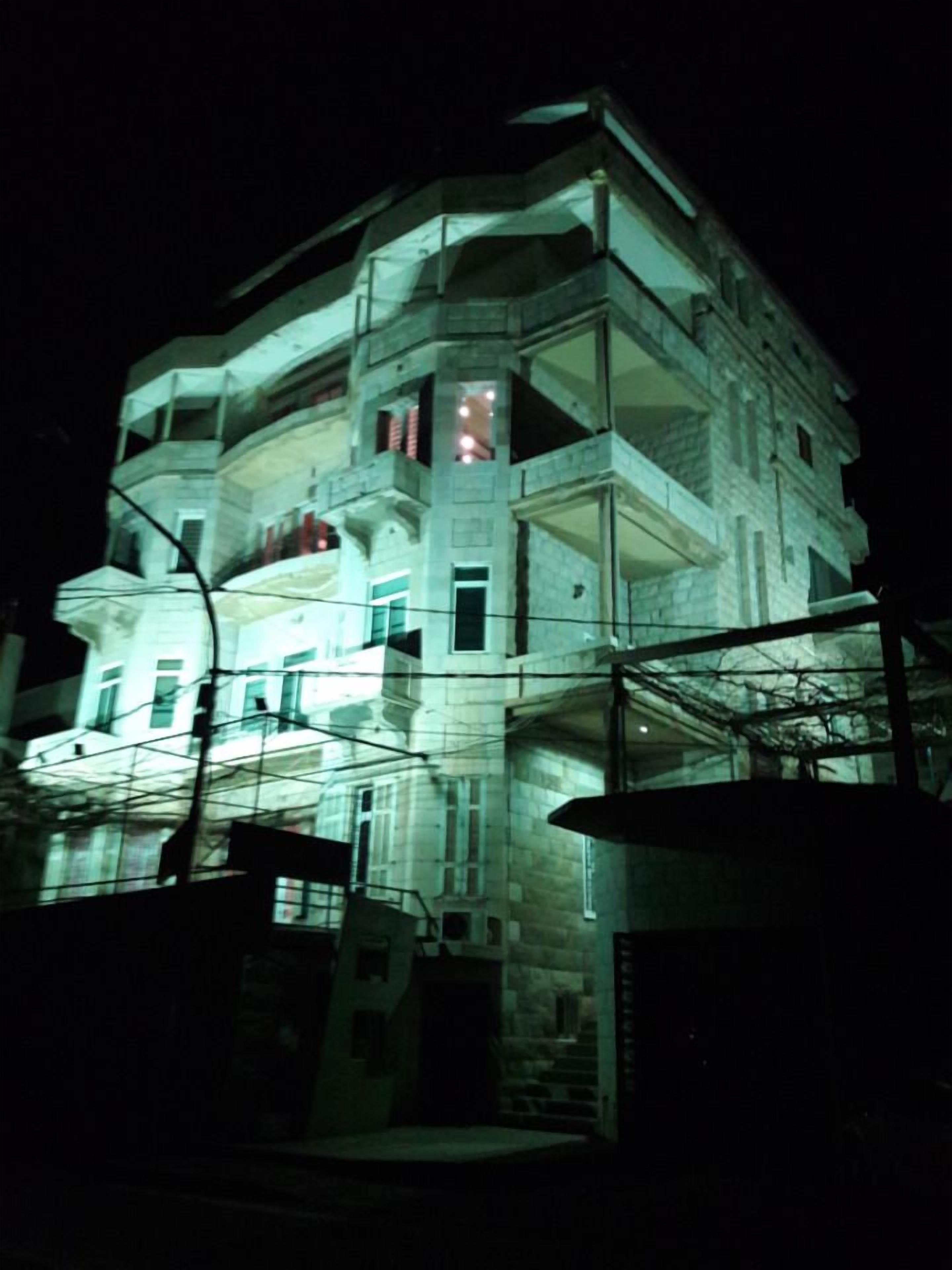 A multi-story building with balconies and large windows, illuminated at night.
