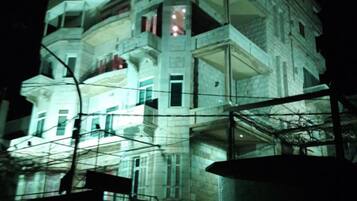 A multi-story building with balconies and large windows, illuminated at night.