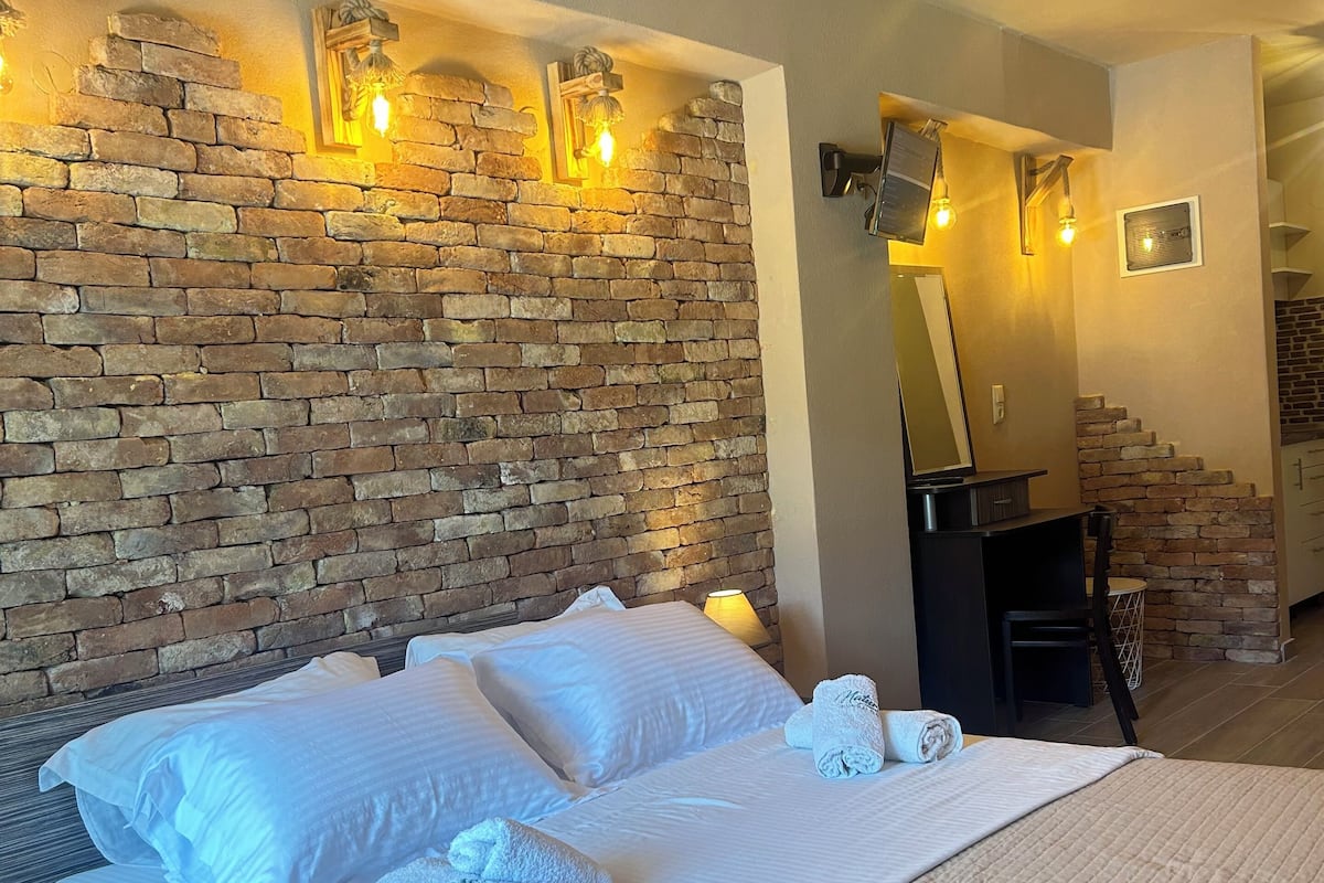 A hotel room with a brick wall, a bed with white linens, and a hanging light fixture.
