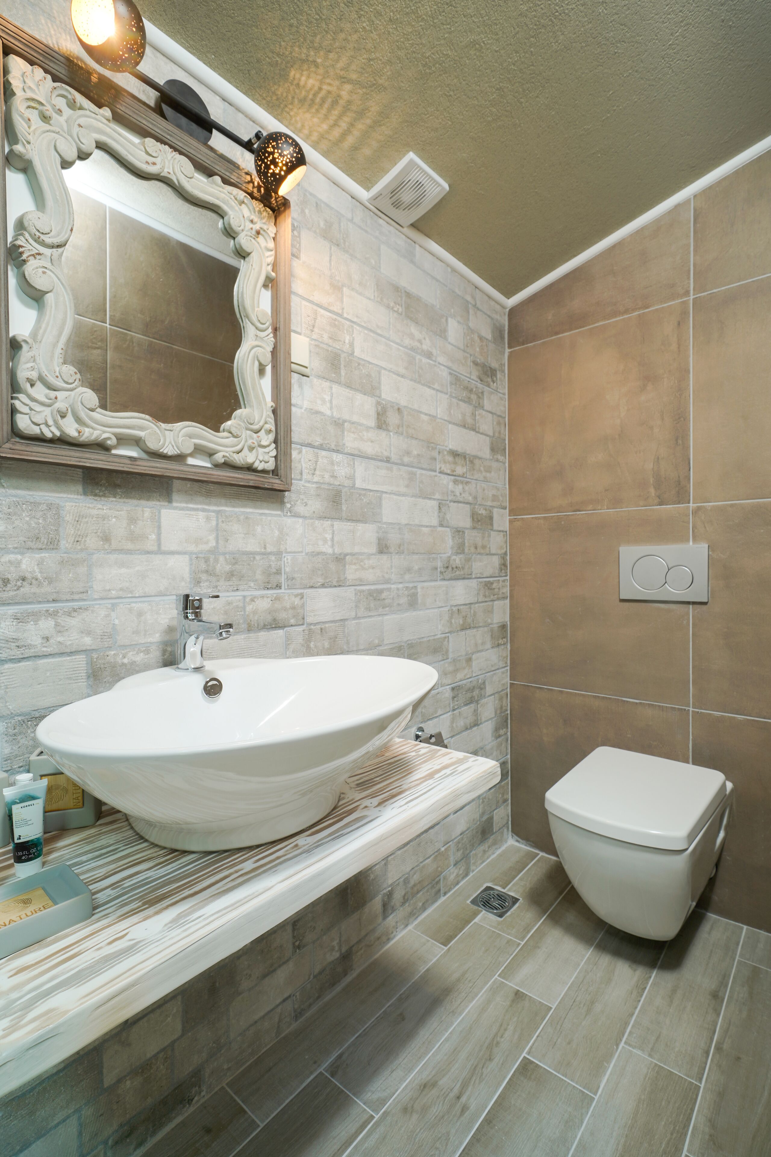 Un baño con un lavamanos grande de color blanco, un inodoro y un espejo con detalles ornamentales.