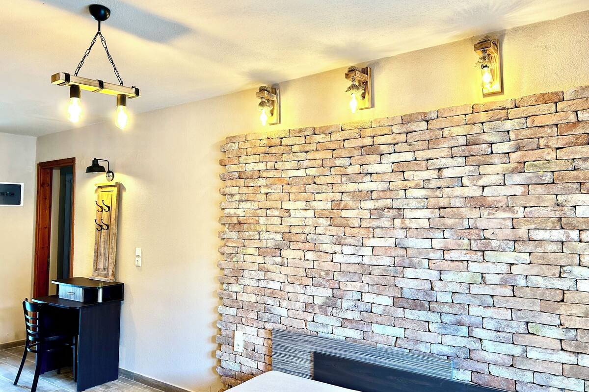 A room with a brick wall, a desk with a chair, and a hanging light fixture.