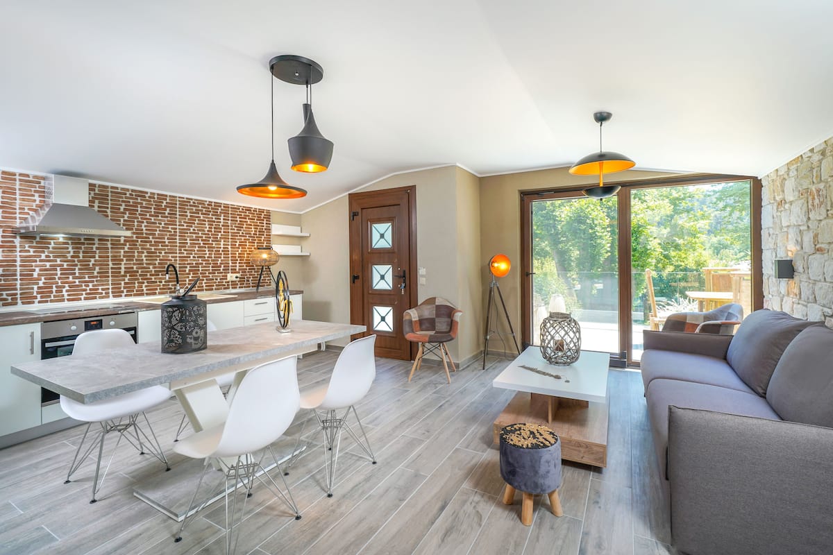 A modern kitchen with a brick backsplash, a dining area with white chairs, and a living room with a sofa and a coffee table.