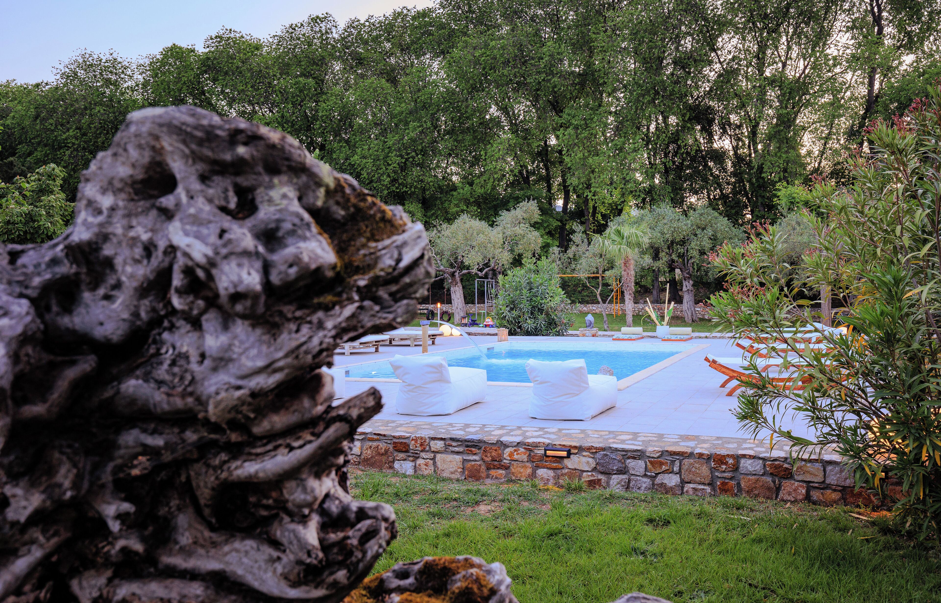 A swimming pool with lounge chairs, surrounded by greenery and a stone wall.