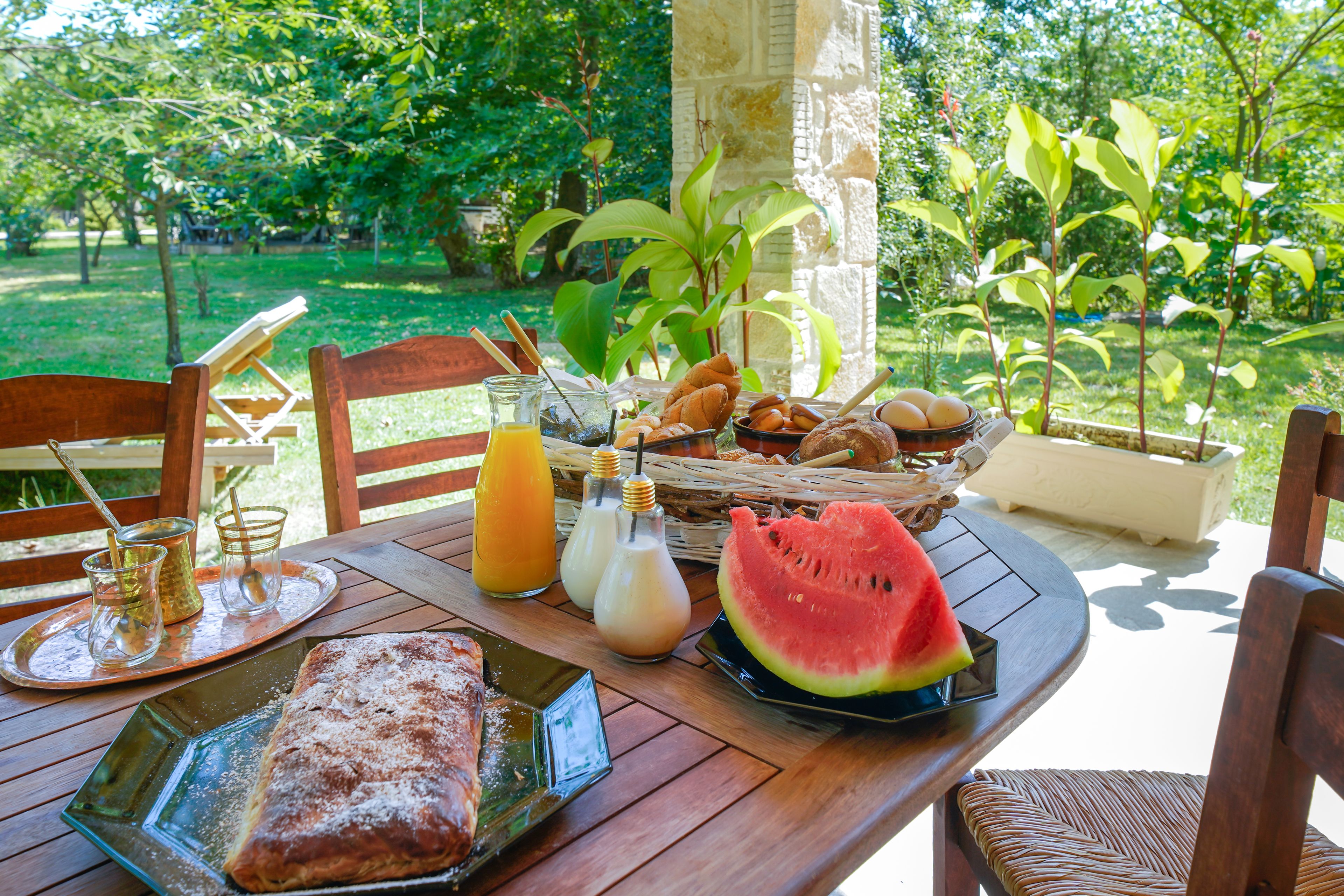 Ein Esstisch mit Gebäck, einem Brotlaib, einem Glas Orangensaft und einem Stück Wassermelone.