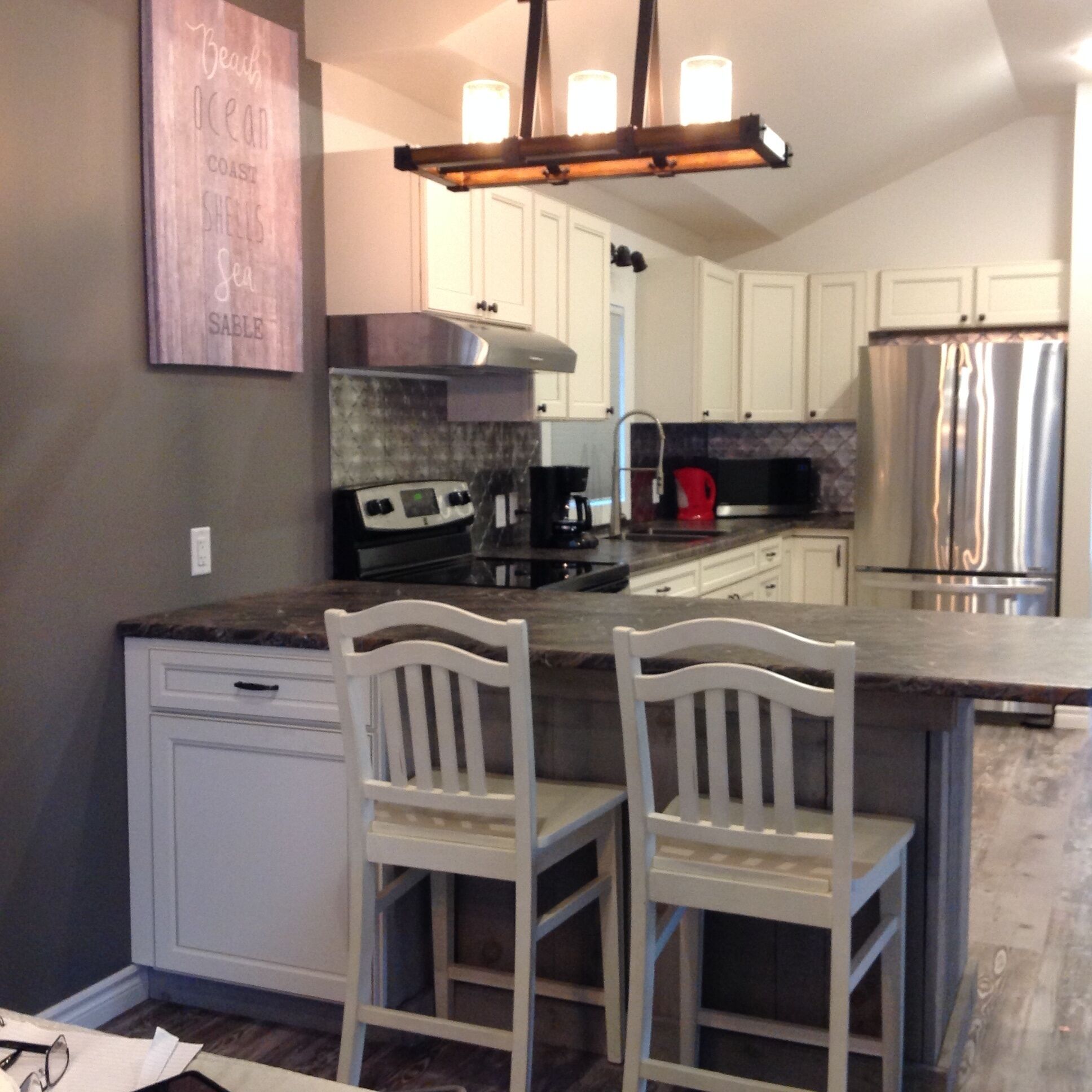 A kitchen with white cabinets, a stainless steel refrigerator, a gas stove, and two white bar stools.