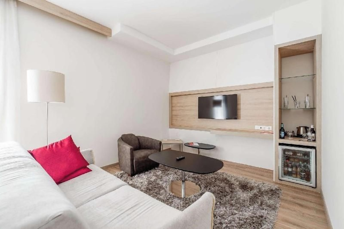 A modern living room with a sofa, armchair, coffee table, TV, and built-in storage.