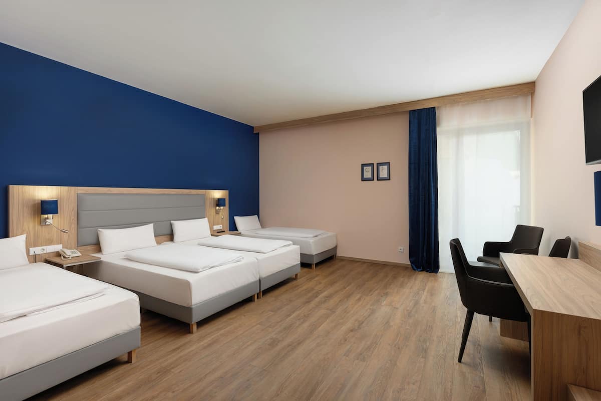 Une chambre d’hôtel avec trois lits, un bureau et une chaise.