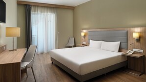 Une chambre d’hôtel équipée d’un lit, d’un bureau, d’une chaise, de tables de chevet, d’une lampe et d’un téléphone.