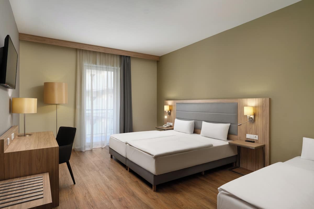 Une chambre d’hôtel avec un lit, un bureau, une chaise, une télévision et une fenêtre avec des rideaux.