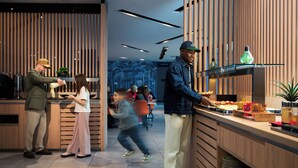 Un intérieur moderne avec un lambris en bois, un comptoir où sont exposés des produits alimentaires et, au fond, un espace détente avec des sièges.